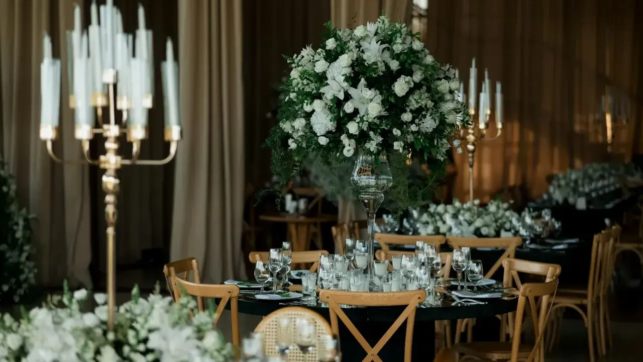 Eleganckie wesele w czarnym stylu. Stoły nakryte czarnymi obrusami, ozdobione białymi kwiatami i złotymi świecznikami.