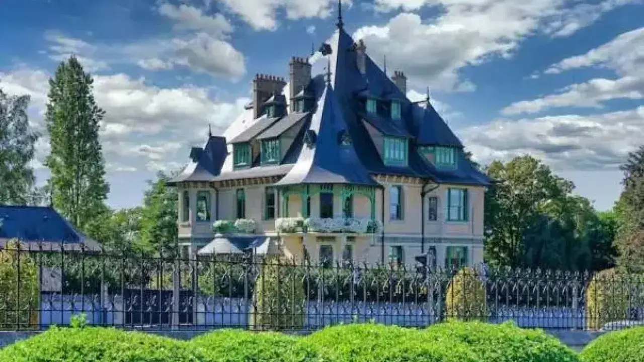 La villa Demoiselle, une demeure de caractère avec ses toits pointus et sa façade claire, se dresse fièrement derrière une grille ouvragée et des buissons taillés.