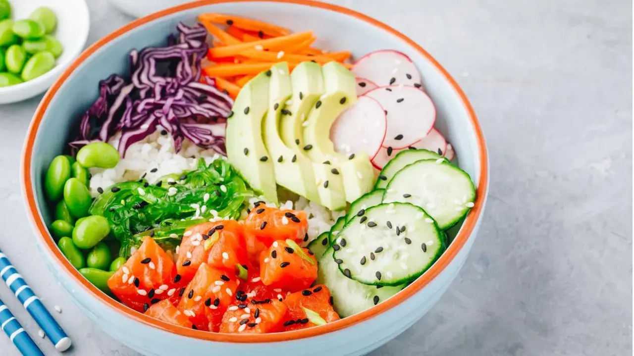 Eine bunte Poke Bowl mit Lachs, Avocado, Edamame, Rotkohl, Gurke, Radieschen und Seetang.
