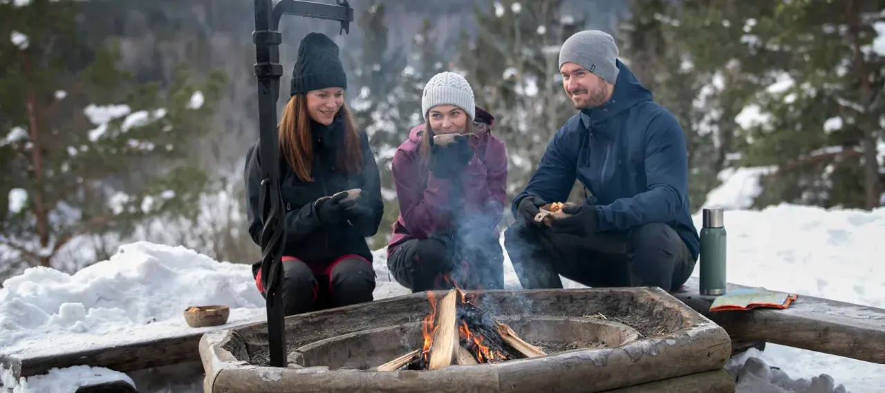 Vänner njuter av värmen från en eld och fika under härliga ute aktiviteter i snöig skogsmiljö.