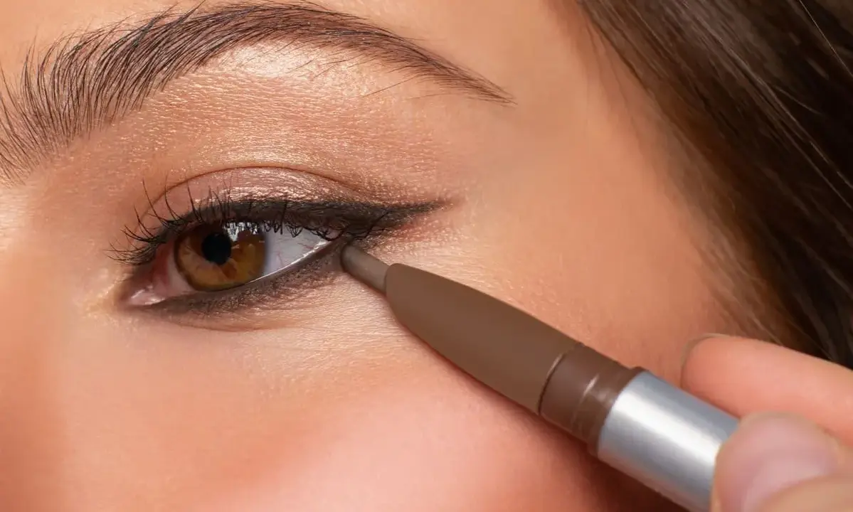 Ojo marrón con delineado invertido, aplicando lápiz marrón en la línea de agua inferior para un look dramático.