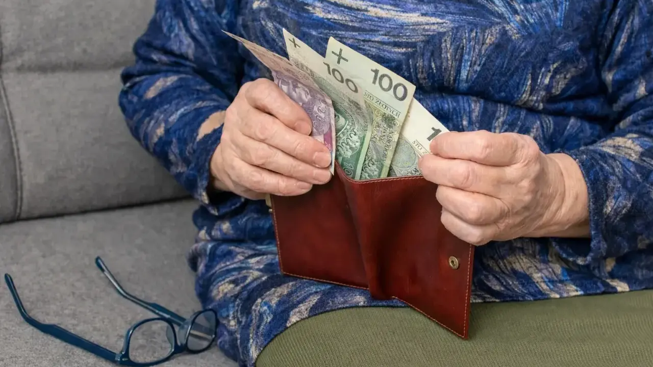 Dłoń starszej osoby wkłada pieniądze do portfela. Widać banknoty 100 zł. To wsparcie dla osób niepełnosprawnych, jak 500 plus dla niepełnosprawnych.