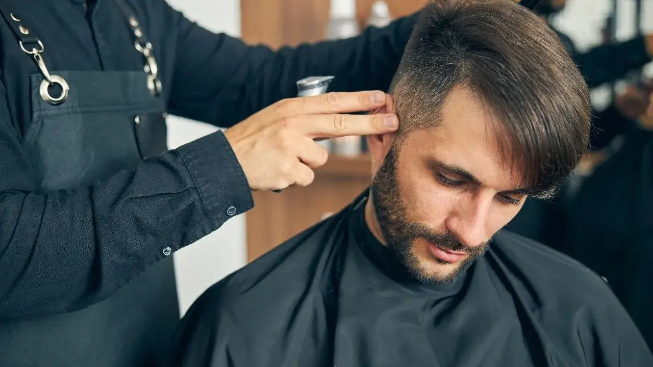 Fryzjer dopracowuje męskie fryzury z grzywką do przodu, tworząc stylowy look.