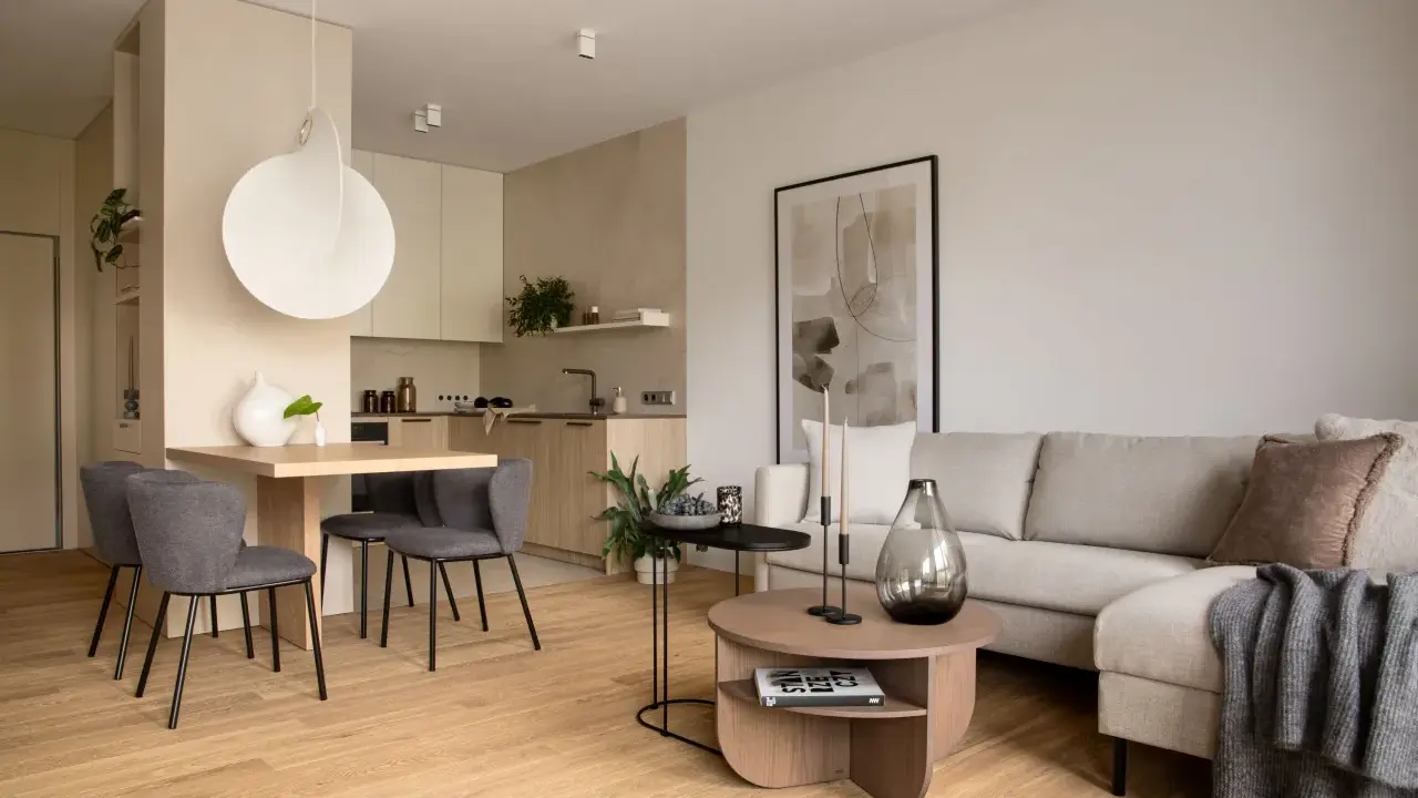 Beżowy salon inspiracje: przytulna przestrzeń z szarą sofą, drewnianym stołem i nowoczesną kuchnią.