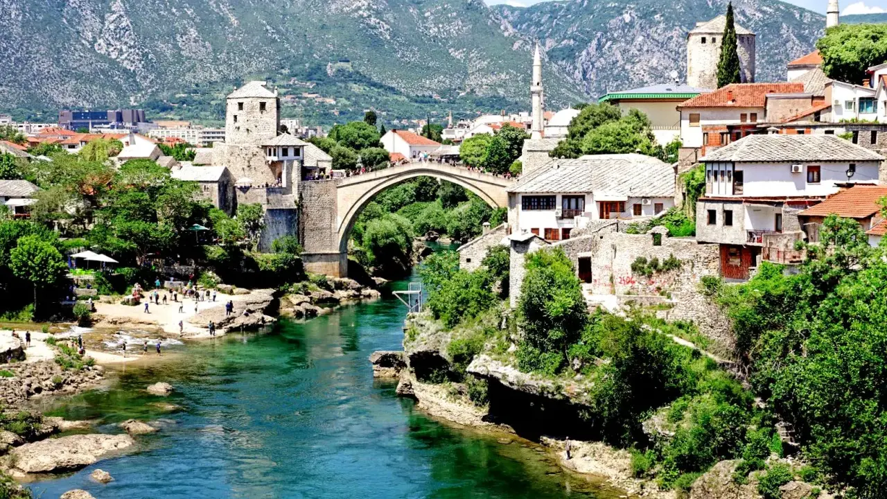 Mostar, Bośnia i Hercegowina: zielona karta dla turystów. Stary Most i rzeka Neretwa w letnim słońcu.