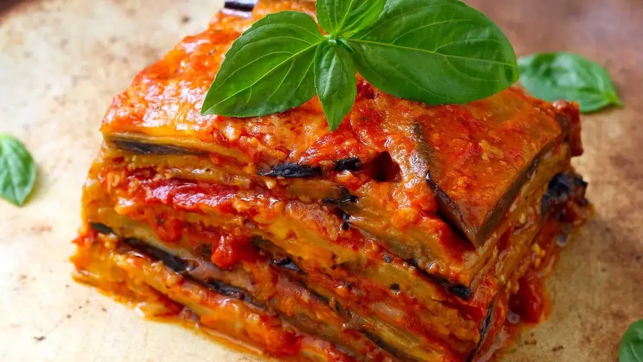Une part généreuse d'aubergine parmigiana, empilée et nappée de sauce tomate, garnie de feuilles de basilic frais.
