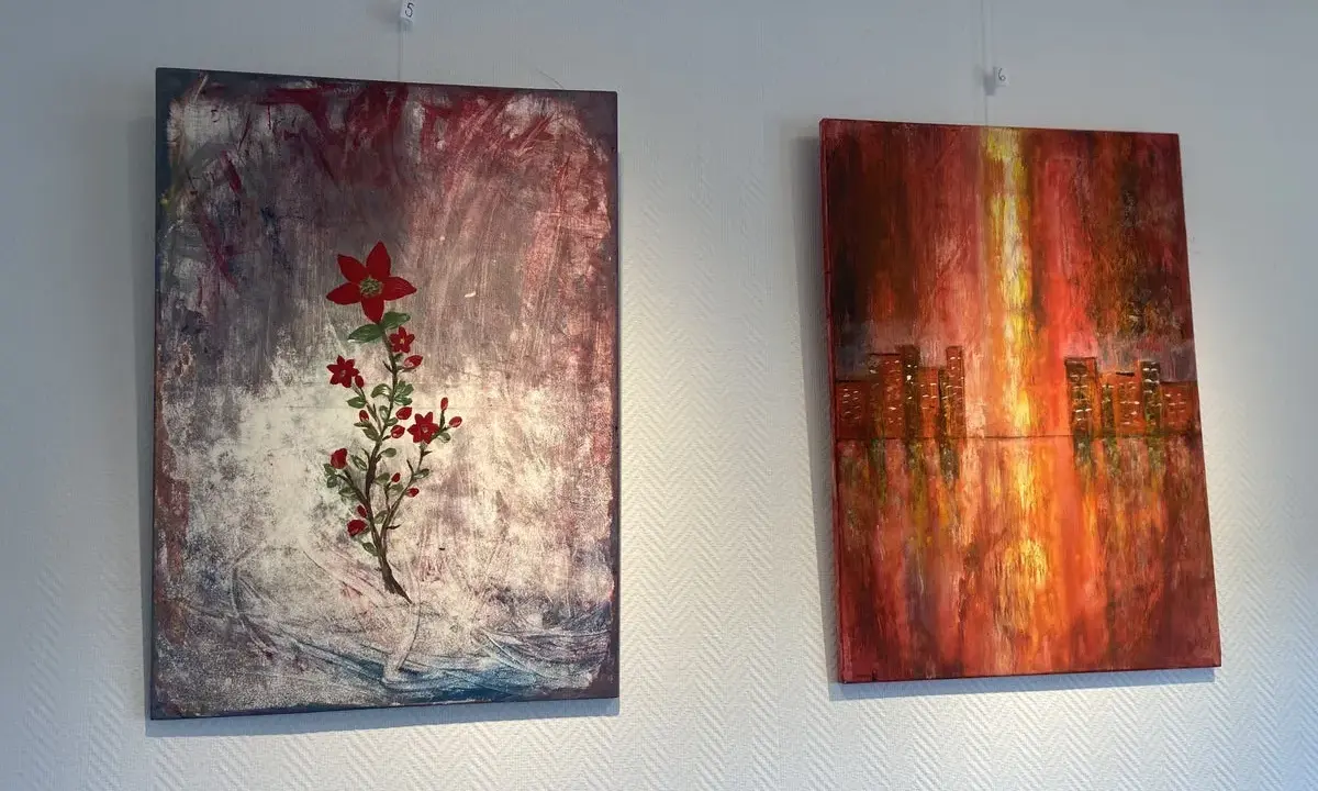 Två abstrakta målningar på väggen. Till vänster en röd blomma på en mörk bakgrund, en fin diy canvas. Till höger en stadssilhuett i varma färger.