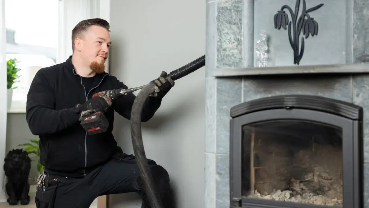 Sotare rengör en braskamin med en dammsugare. Frågar du dig "vad kostar sotning av braskamin"?