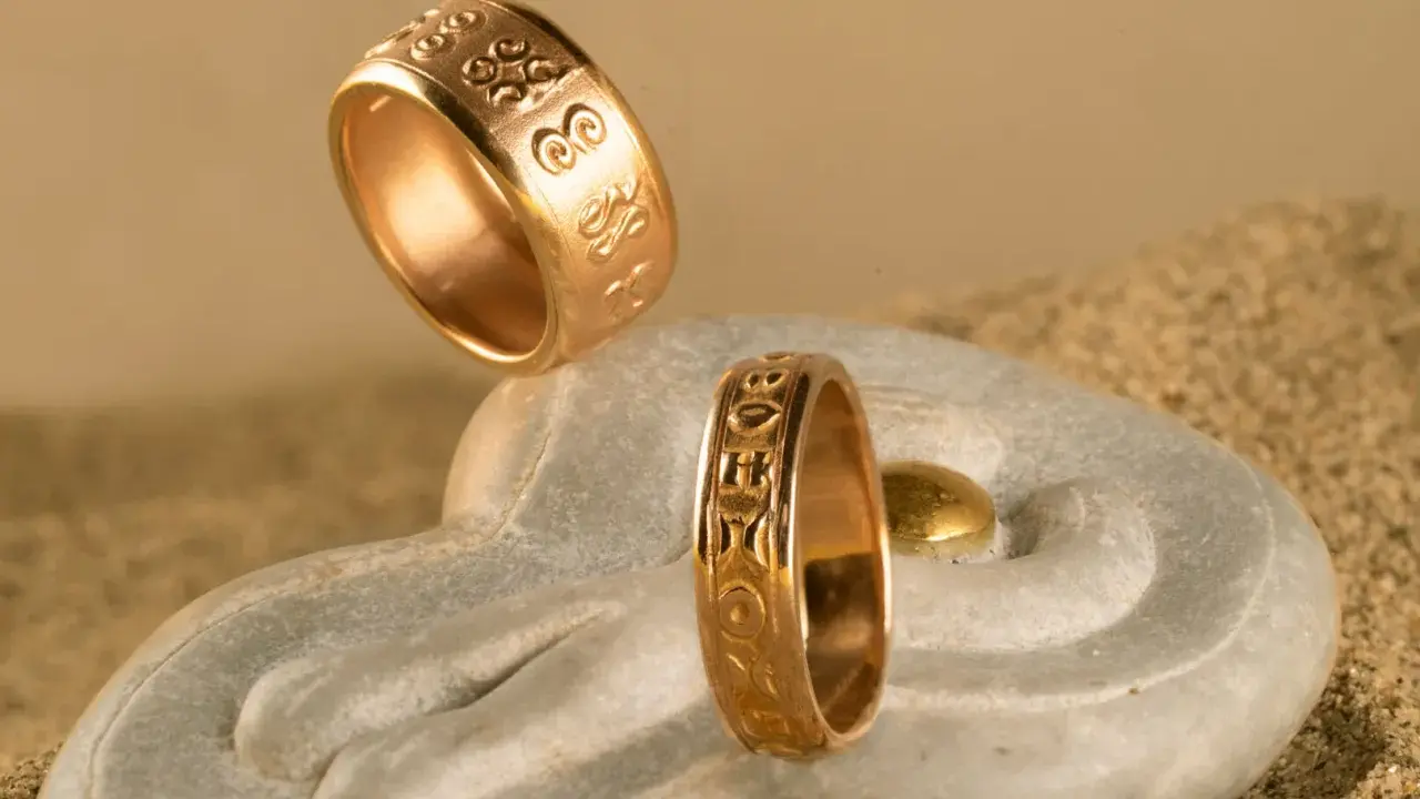 Due anelli d'oro con incisioni uniche, che mostrano diversi tipi di fedi nuziali, su una pietra a forma di mano con sabbia.