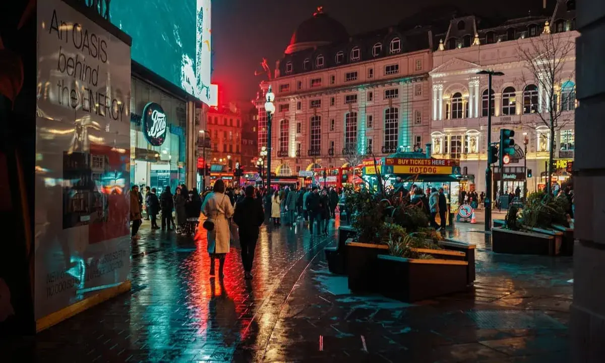 Luci al neon e riflessi sull'asfalto bagnato, la vibrante vita notturna londra pulsa tra la folla e gli edifici storici illuminati.