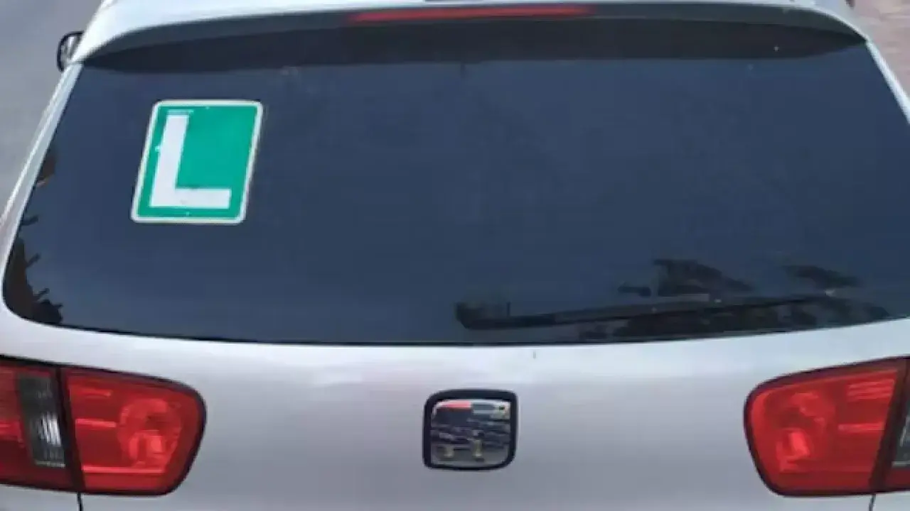 El coche tiene una L verde en la ventana trasera, indicando que el conductor está aprendiendo.
