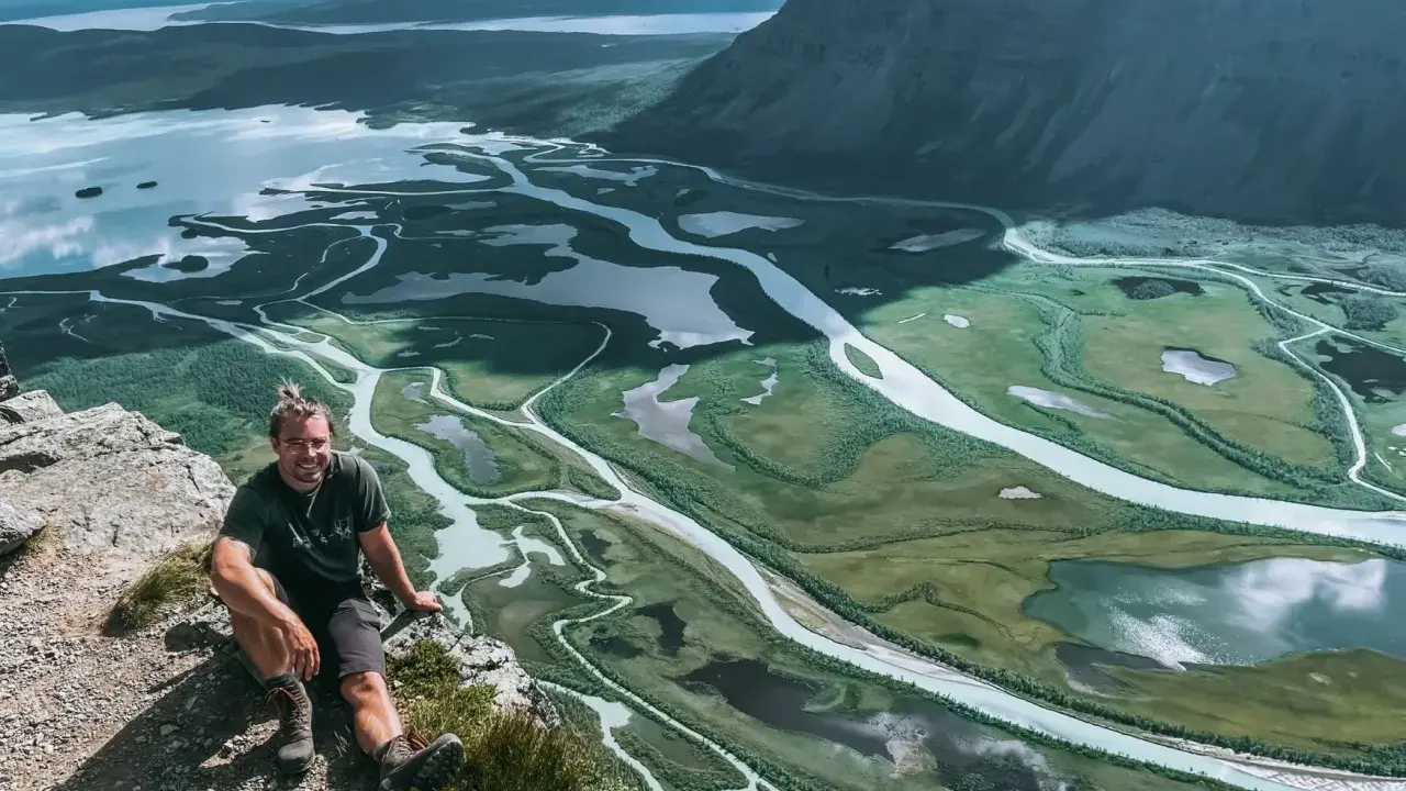 Man sitter på en klippa med en fantastisk utsikt över ett meandrande vattendrag och fjällandskap i Sarek. Aktse till skierfe!