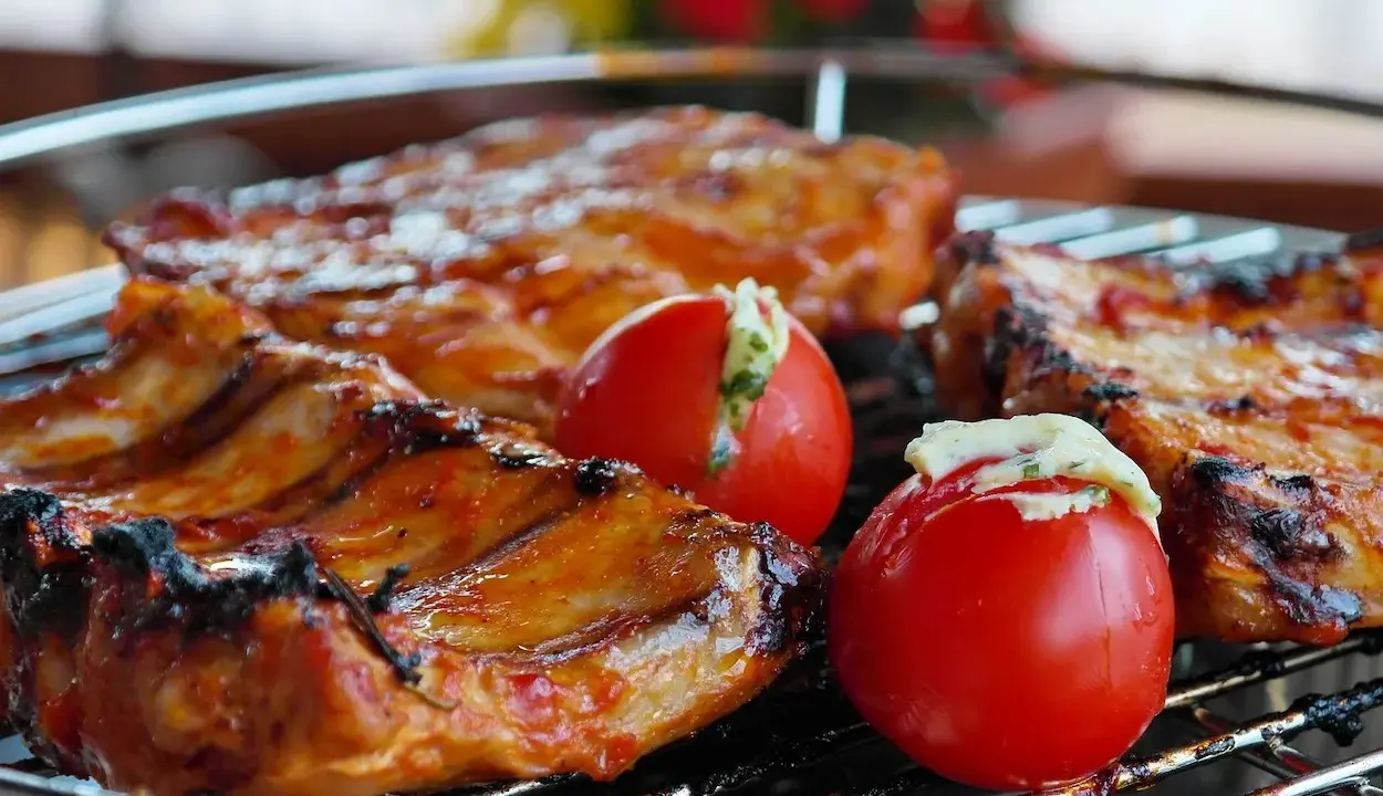 Costillas de cerdo y tomates rellenos en una parrilla. El tiempo que tarda el carbón en hacer brasa es clave para esta deliciosa cocción.