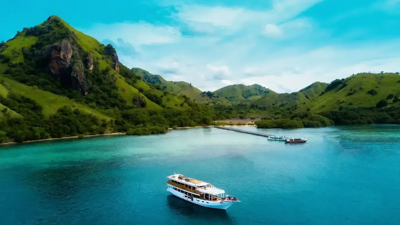 Un'isola lussureggiante con colline verdi e un mare turchese, dove si trova Bali, con una nave da crociera che naviga nelle acque cristalline.