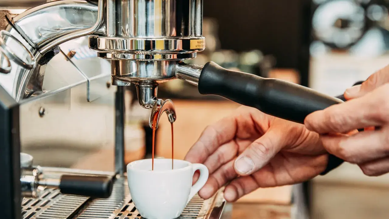 Frisch gebrühter Kaffee fließt aus der Espressomaschine in eine kleine Tasse.
