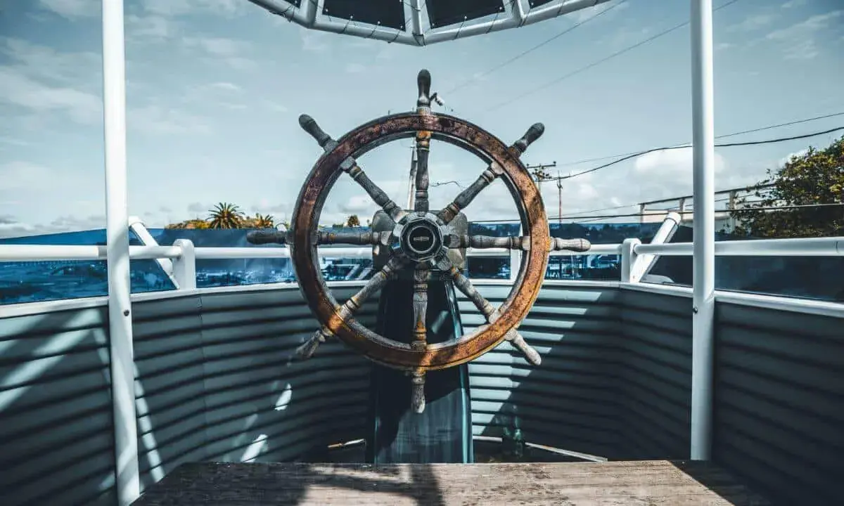Roue de gouvernail en bois patiné, prête à barrer un bateau vers l'horizon bleu.