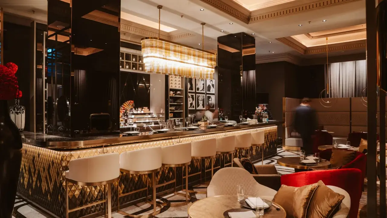 Elegante Bar mit goldenen Akzenten, weißen Barhockern und stilvollen Sitzbereichen. Ein Ort, der zu den besten Restaurants in Berlin passt.