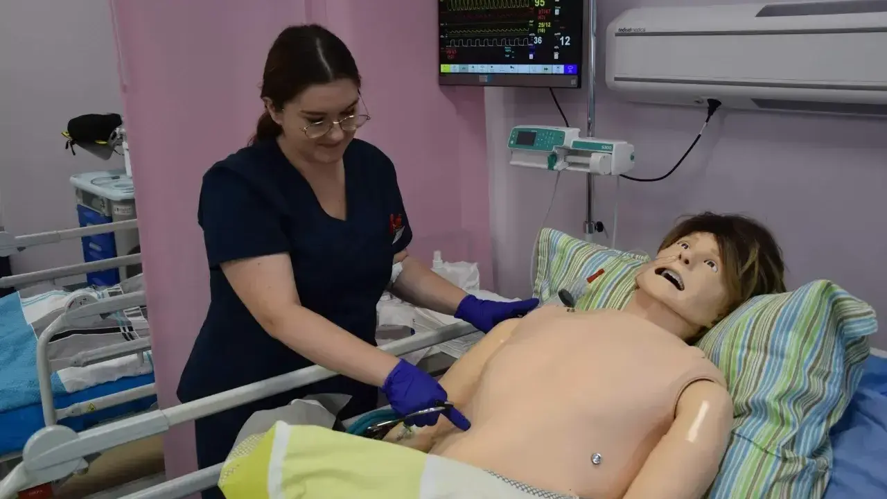 Studentka stomatologii ćwiczy procedury medyczne na fantomie. Monitor parametrów życiowych pokazuje dane.
