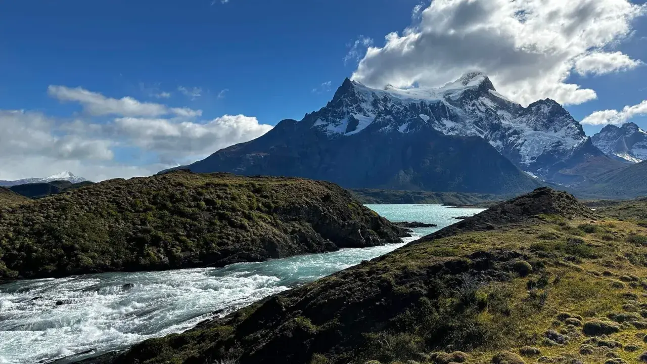Wodospad w **Torres del Paine** z turkusową wodą i ośnieżonymi szczytami w tle.
