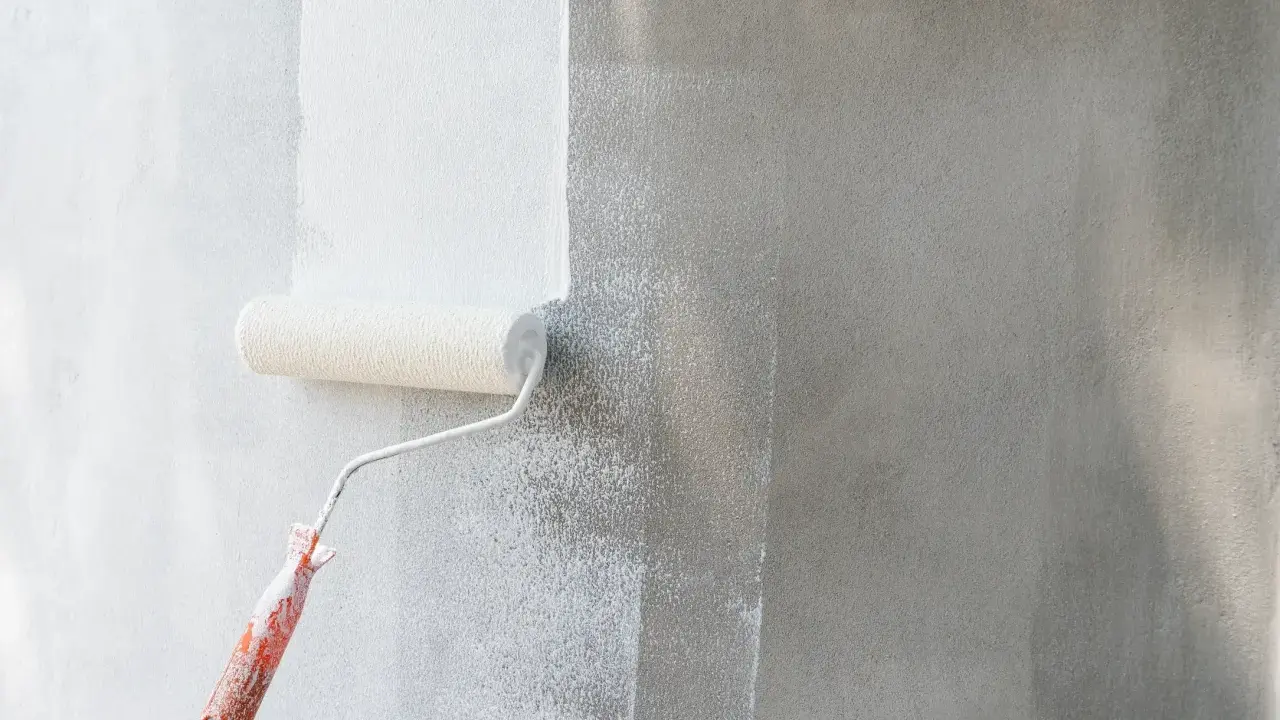 Rodillo blanco aplica pintura a pared gris. Se ve el proceso de cuantas manos de pintura se le da a una pared para un acabado perfecto.