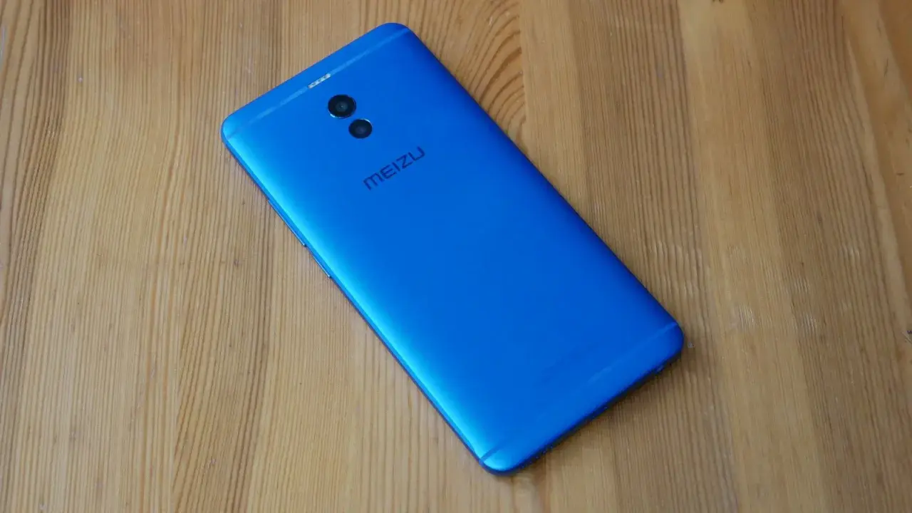 Niebieski smartfon Meizu M6 Note z podwójnym aparatem z tyłu leży na drewnianym blacie.