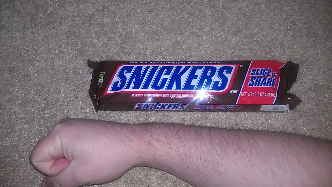 Opakowanie Snickers Slice 'n Share, obok ludzkiej ręki. Zastanawiasz się, snickers ile kalorii?