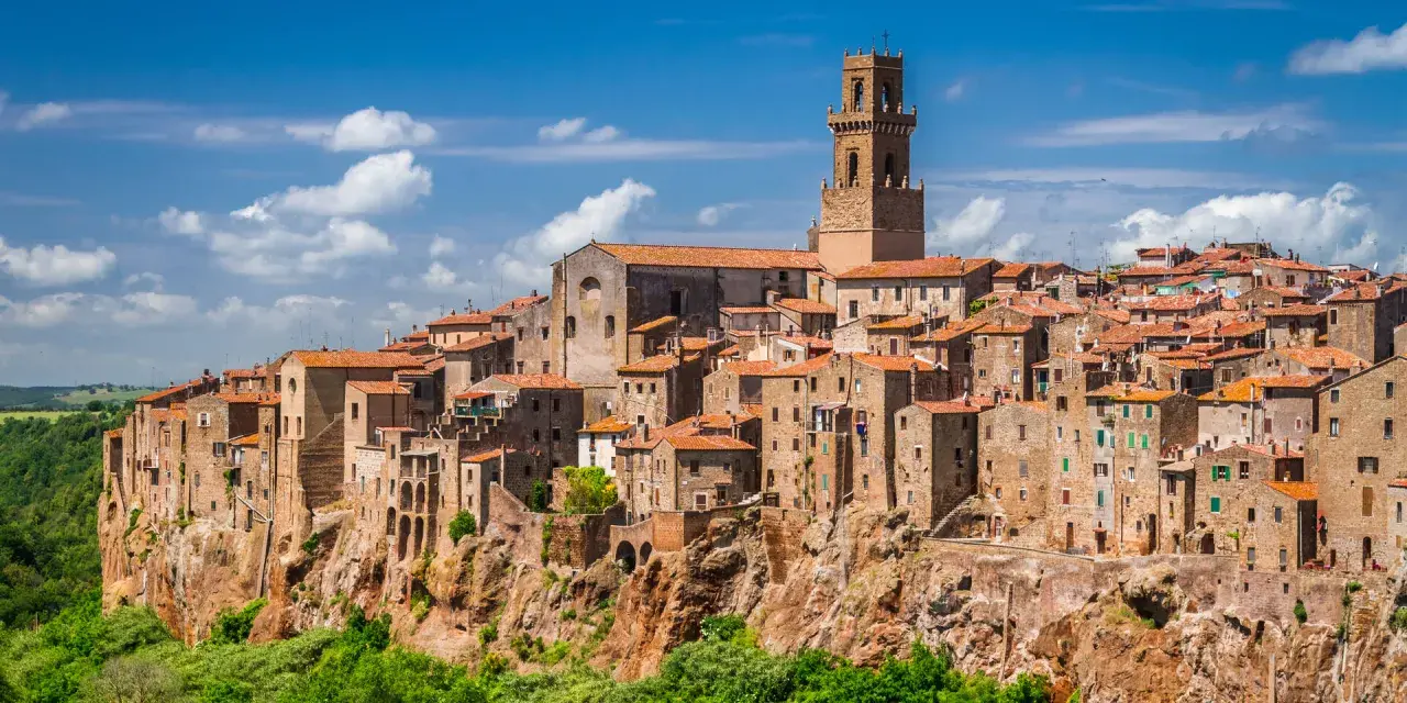 Eine malerische Stadt in der Toskana thront auf einem Felsen, umgeben von grünen Hügeln und blauem Himmel mit Wolken.