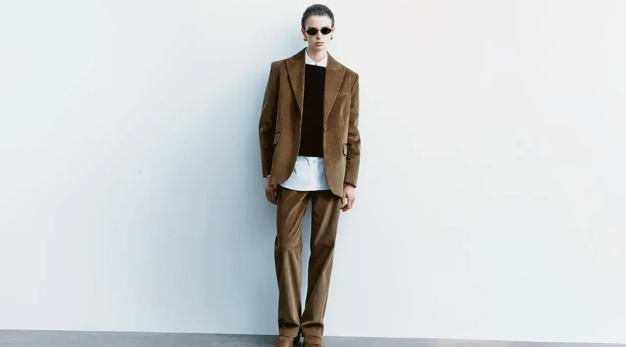 Model in a brown corduroy suit, white shirt, and black sweater, wearing sunglasses.