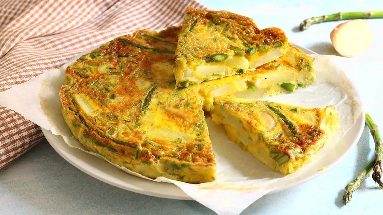 Una gustosa frittata di asparagi, con patate e uova dorate, tagliata a fette su un piatto bianco.