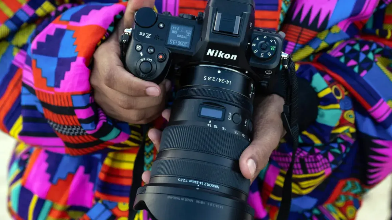 Aparat fotograficzny lustrzanka Nikon Z9 z obiektywem NIKKOR Z 14-24mm f/2.8 S, trzymany przez osobę w kolorowej, wzorzystej kurtce.