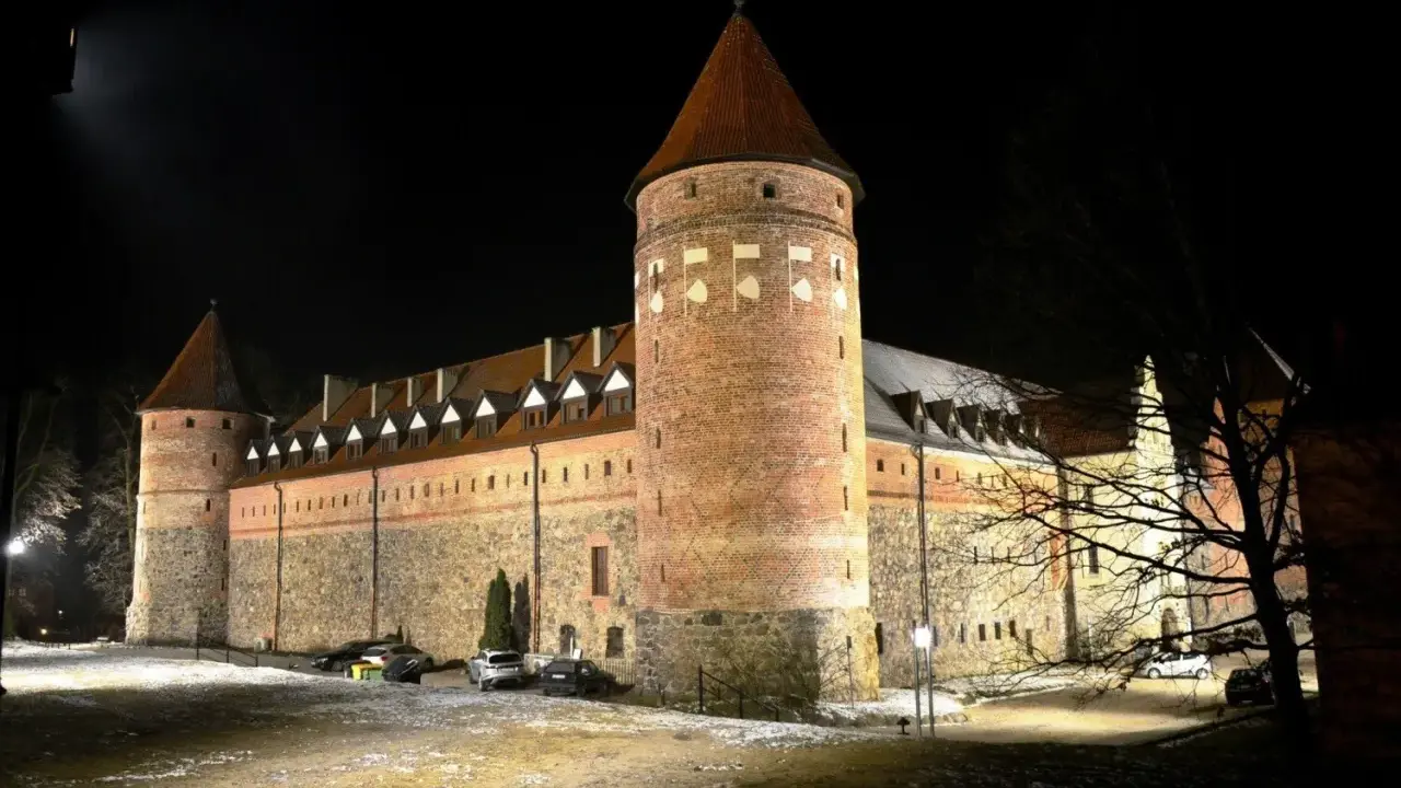 Zamek w Bytowie nocą, oświetlony, z wieżami i kamiennymi murami.