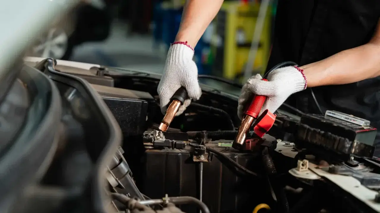 Manos enguantadas conectando cables a la batería del coche. Es hora de desconectar la batería del coche para un mantenimiento seguro.