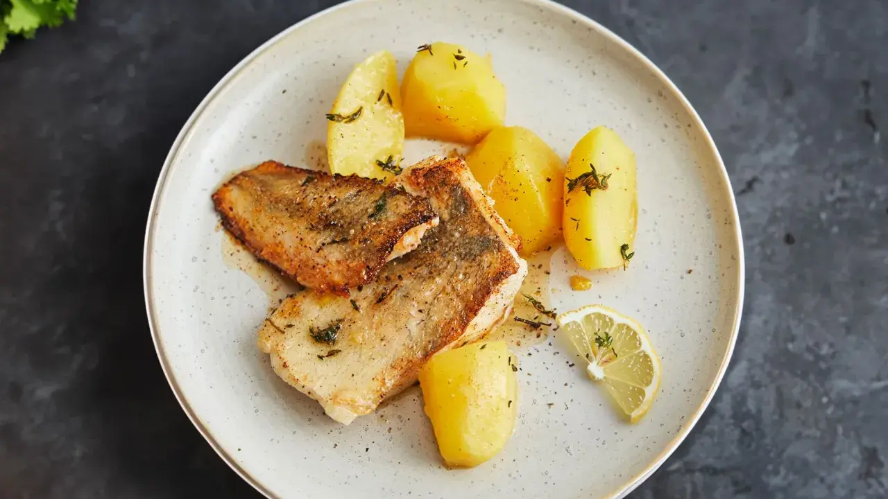 Gebratener Seehecht mit Haut, serviert mit Salzkartoffeln und Zitrone. Ein köstliches Gericht, das zeigt, wie man Seehecht mit Haut zubereitet.
