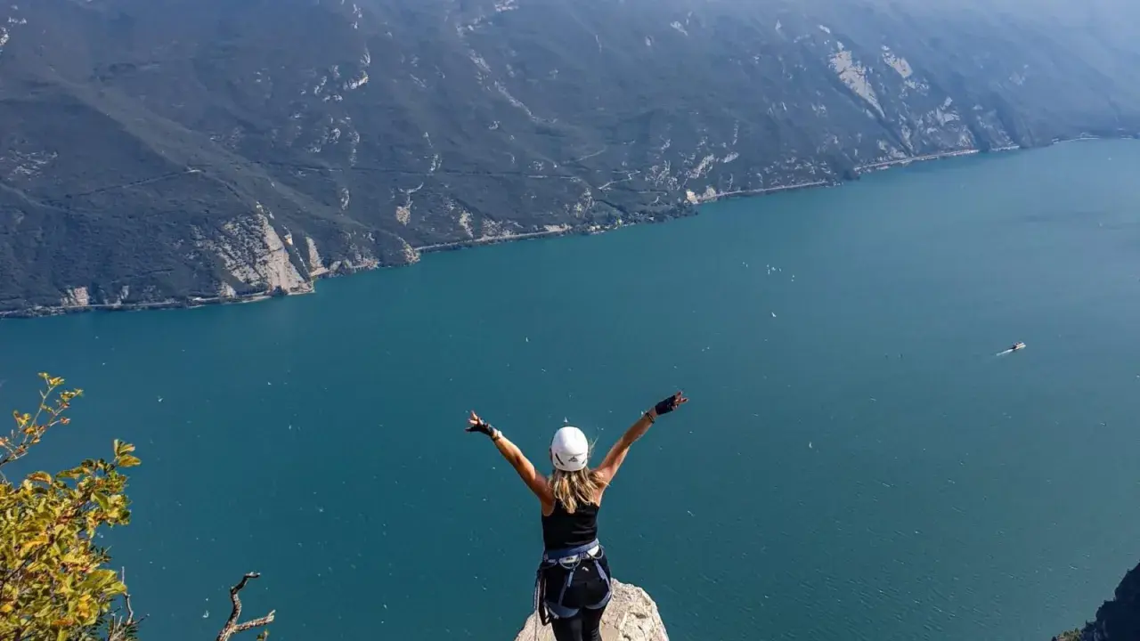 Kobieta z rękami w górze na szczycie klifu, podziwiająca jezioro Garda po przejściu via ferrata.