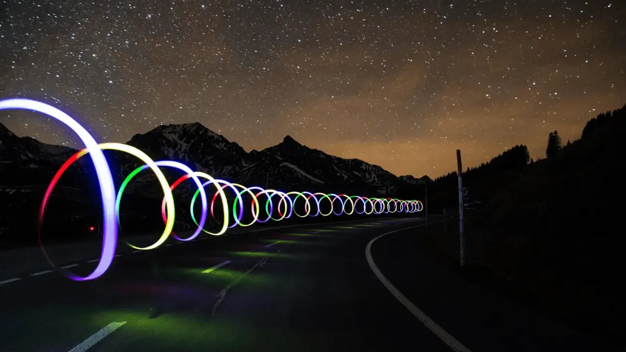 Una carretera nocturna bajo un cielo estrellado, con aros de luz de colores que parecen flotar. ¡Trucos fotos geniales!