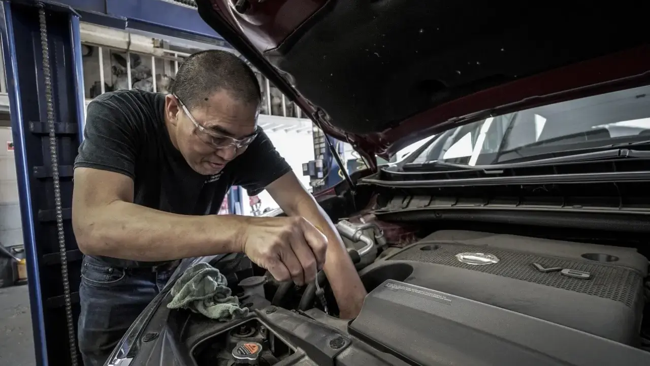 Mechanik w okularach ochronnych pracuje przy silniku samochodu. Zastanawiasz się, ile kosztuje wymiana oleju?