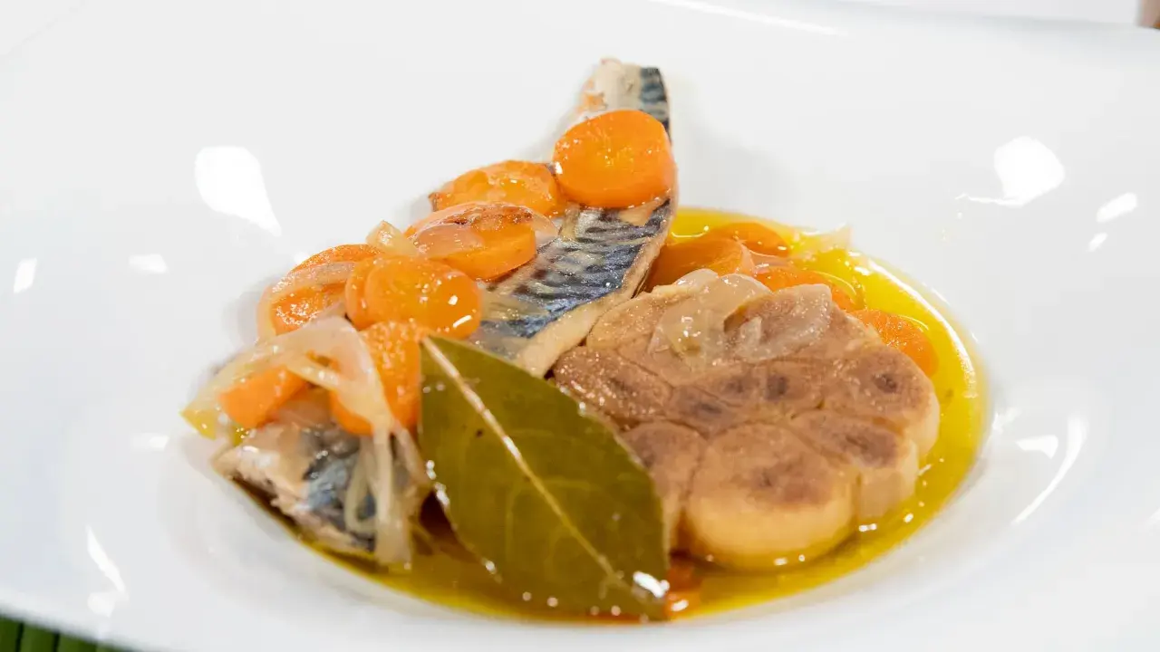 Deliciosa caballa en escabeche con zanahorias, cebolla y laurel en un plato blanco.