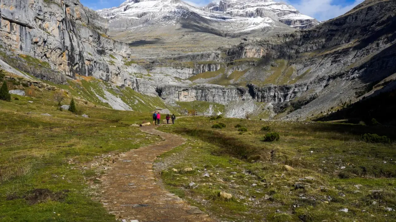 Wanderer auf einem Pfad im Ordesa Nationalpark, umgeben von steilen Felswänden und schneebedeckten Gipfeln.
