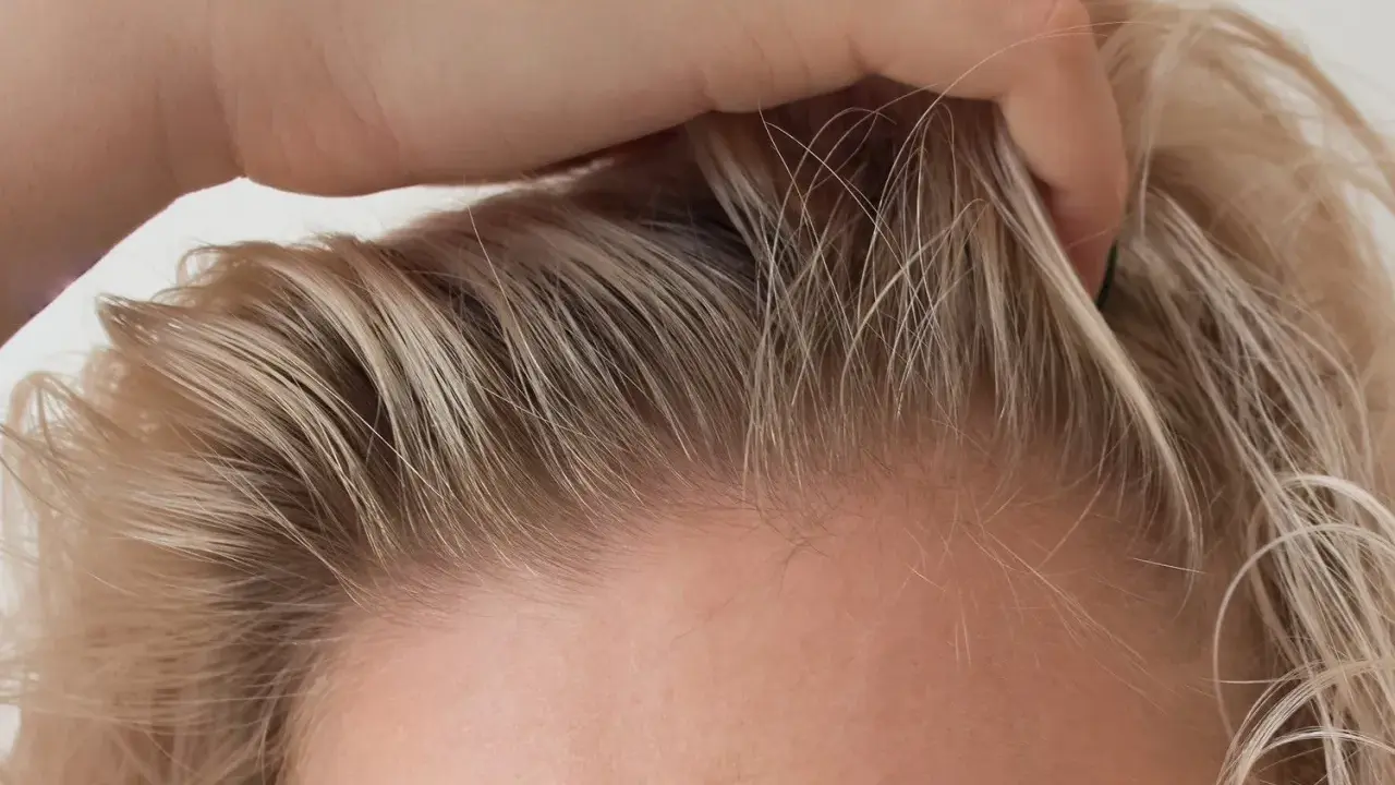 Dłoń delikatnie przeczesuje jasne włosy, ukazując drobne kosmyki, które zdradzają, jak ujarzmić baby hair.