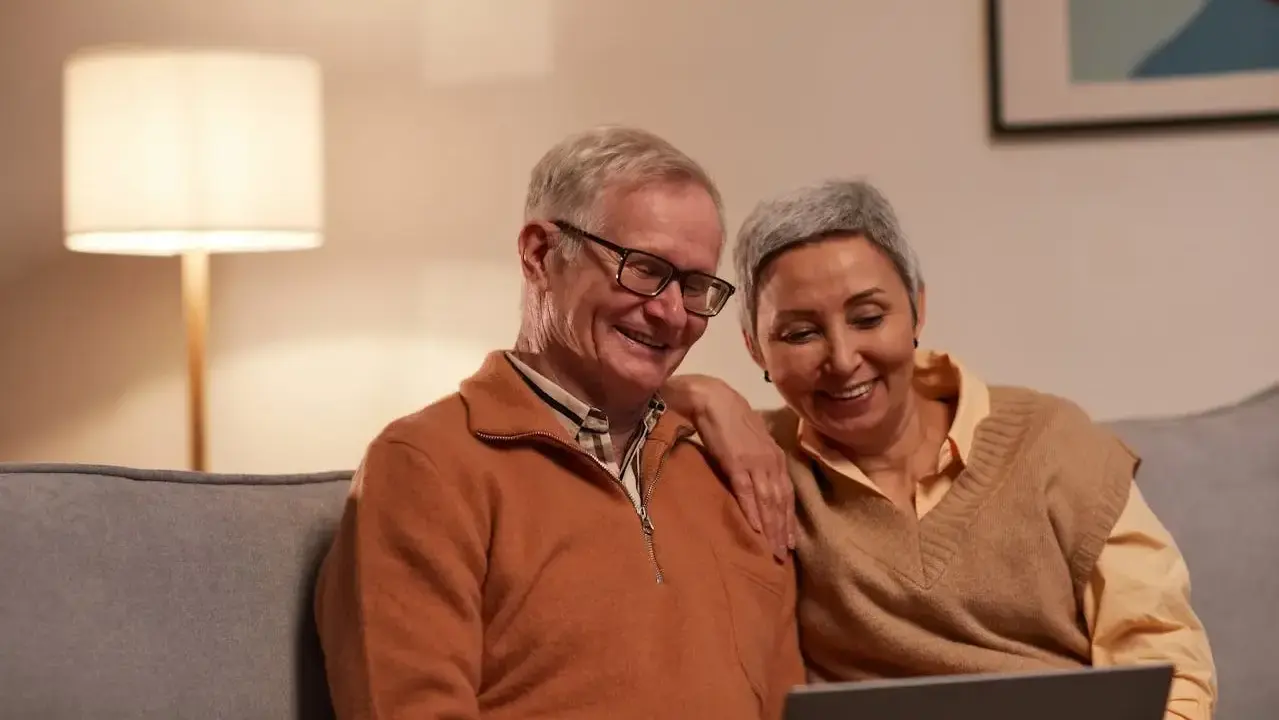 Uśmiechnięta para seniorów przegląda coś na laptopie, być może szukając informacji, czy chorobowe wlicza się do emerytury KRUS.