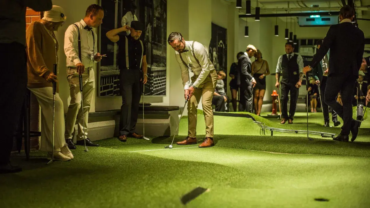 Människor i festliga kläder spelar minigolf på Golfbaren Stockholm.