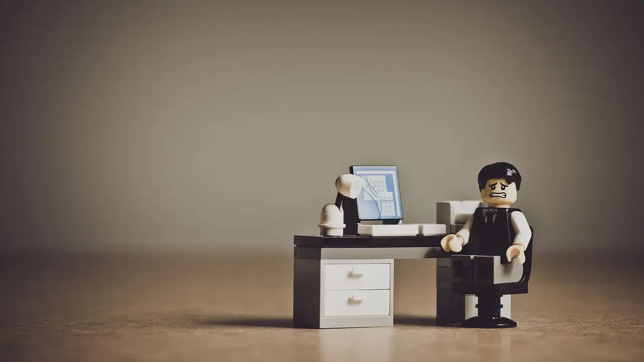Figurka Lego przedstawiająca zestresowanego pracownika siedzącego przy biurku z komputerem.