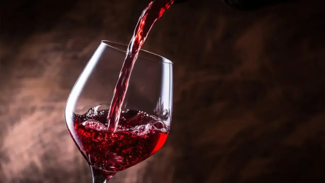 Vino tinto se vierte en una copa, creando burbujas y espuma. Un brindis por el día del vino.