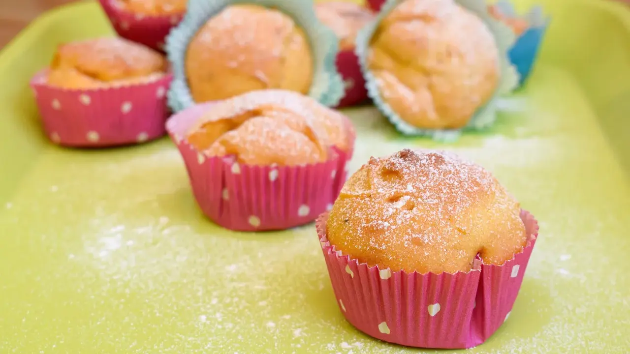 Leckere Muffins ohne Ei, bestäubt mit Puderzucker, in bunten Papierförmchen auf hellgrüner Unterlage.