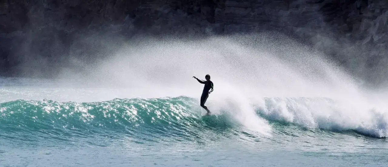 Surfer in Aktion auf einer Welle an der Algarve. Die Gischt spritzt, während er die portugiesische Küste genießt.