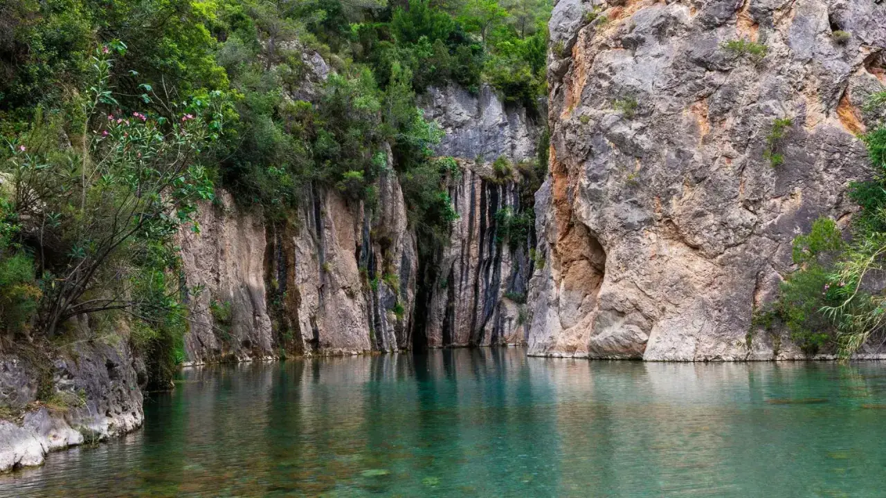 Aguas cristalinas reflejan imponentes rocas y vegetación exuberante en estas piscinas naturales de Castellón. Un rincón idílico para refrescarse.