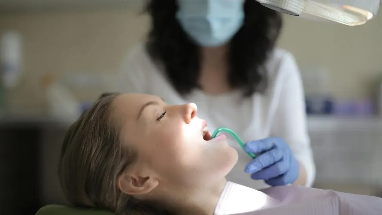 Pacjentka u dentysty, która ma w ustach zieloną końcówkę ssaka stomatologicznego.