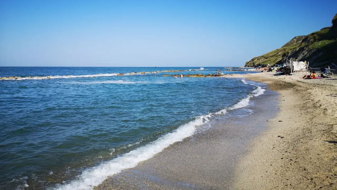 La **spiaggia** di **Castel di Mezzo** baciata dal sole, con il mare azzurro e la collina verde sullo sfondo.