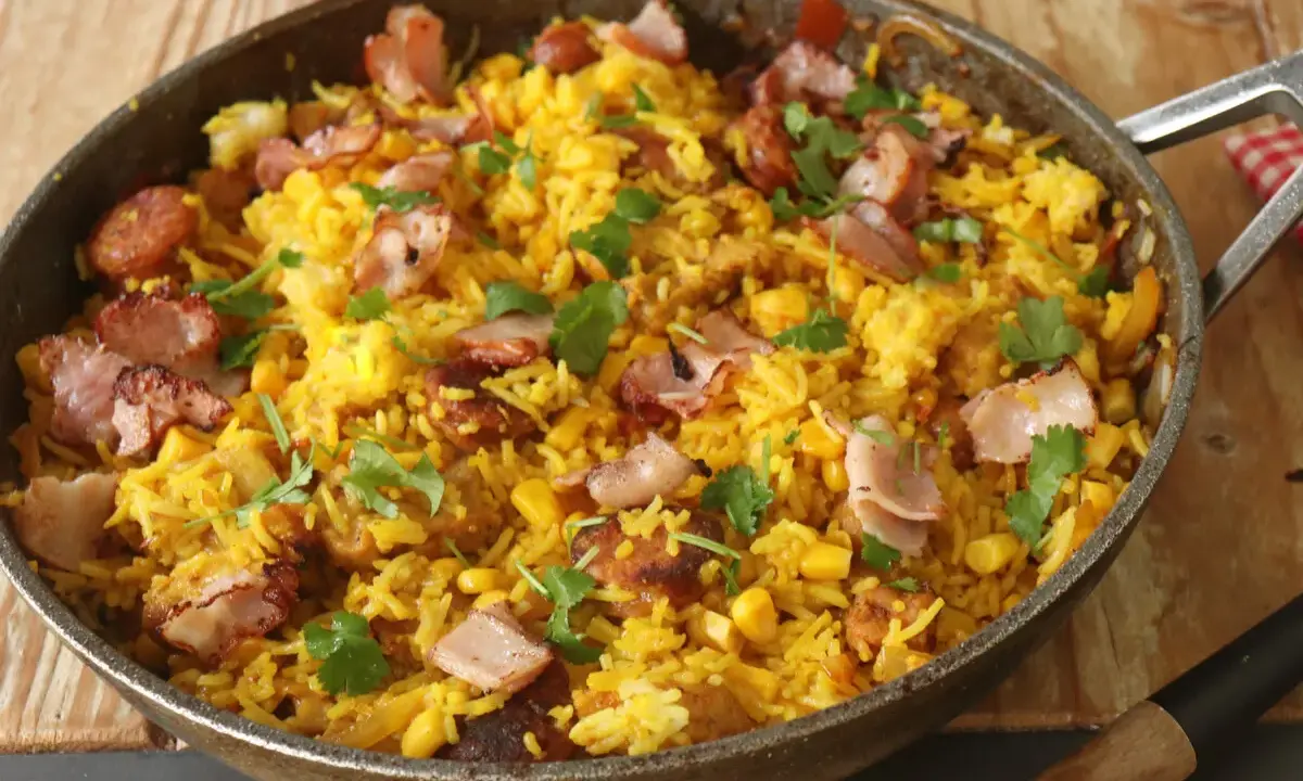 Arroz paisa en sartén, con trozos de tocino crujiente, maíz y cilantro fresco. ¡Un festín para los sentidos!