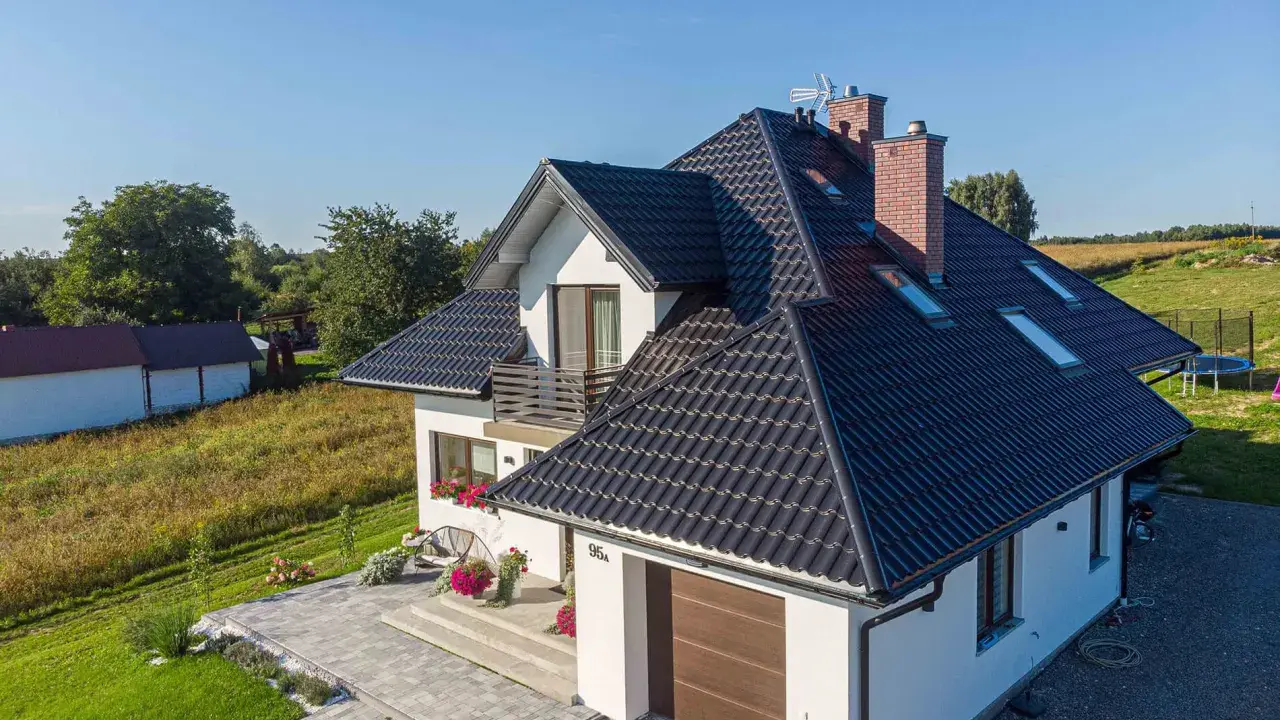 Nowoczesny dom z czarnym dachem, odpornym na warunki atmosferyczne, klasa korozyjności C4. Otoczony zielenią i zadbanym podjazdem.